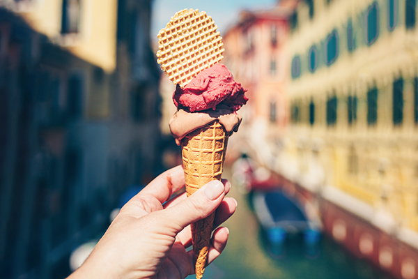 A hand holds a gelato cone with Italian street in background