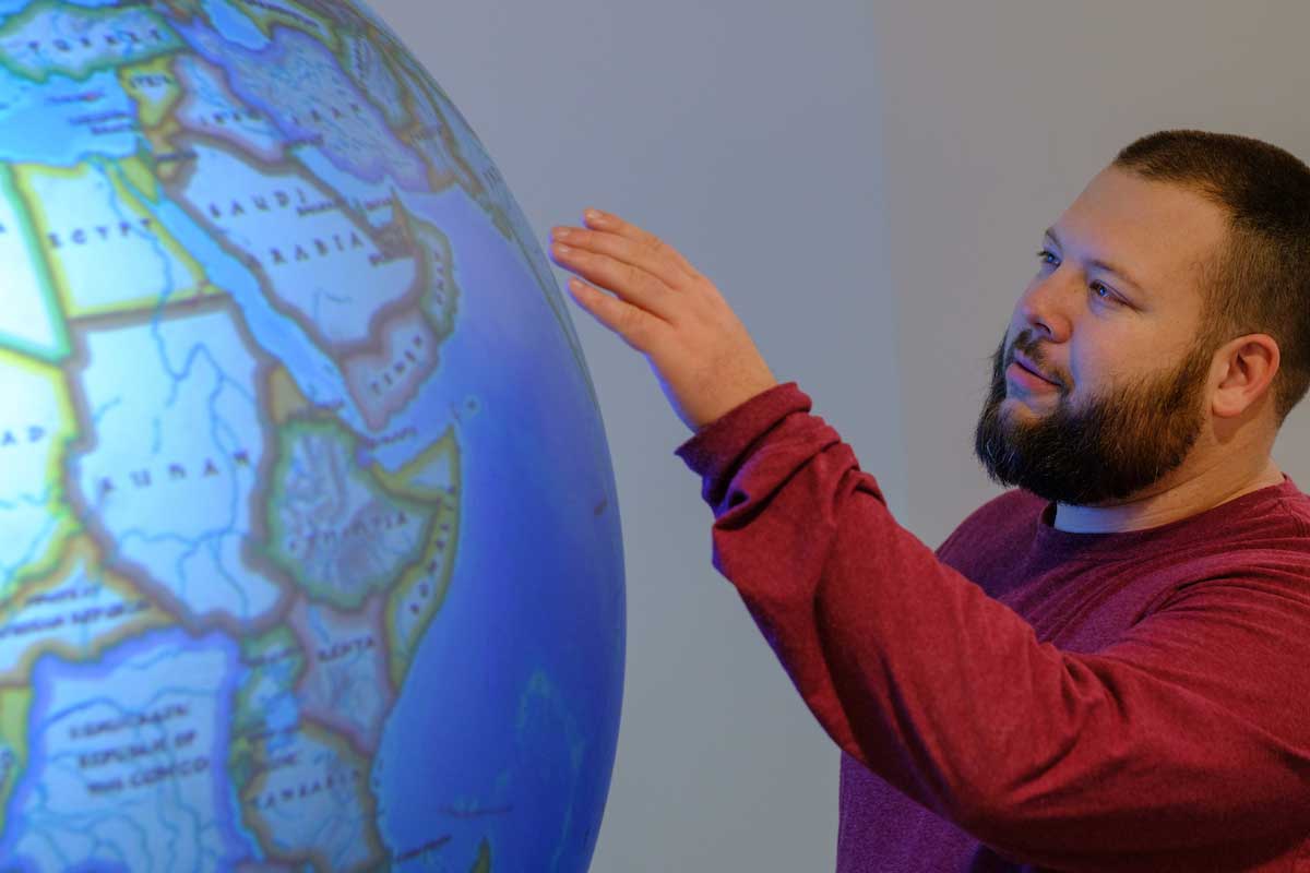 A student wearing a red shirt gently touches a large illuminated globe displaying Africa, the Middle East, and parts of Europe and Asia, with focused attention.