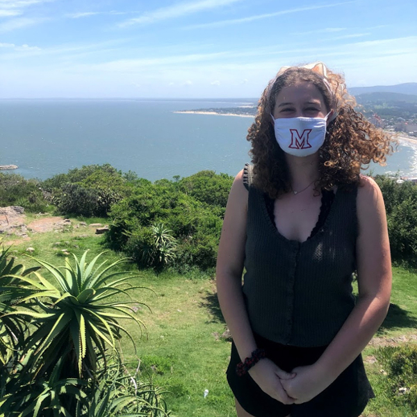 Anna wears a Miami facemask while standing in front of beautiful scenery in Uruguay
