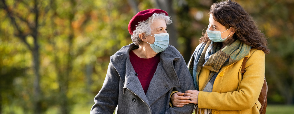 Two women wearing face masks. The younger one appears to be assisting the older one