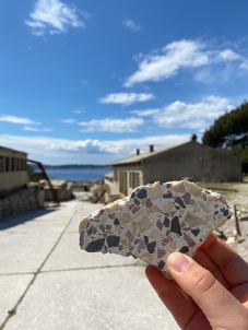 Hand holding up Goli Otok tile with land and water in background