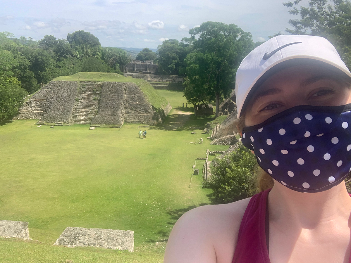 A pyramid is visible in the background. Grace stands close to camera and wears a face covering