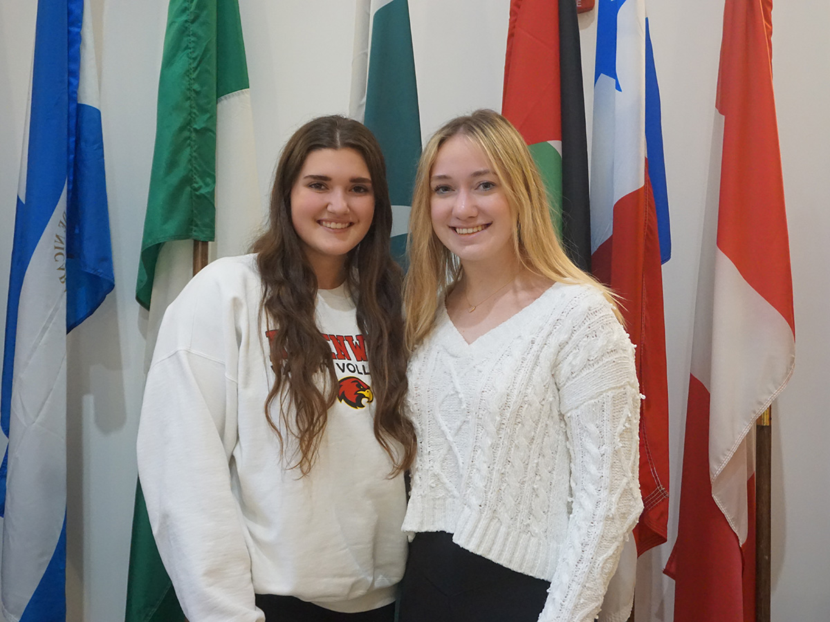 Lana and Maddy pose next to the MacMillan Hall International flags