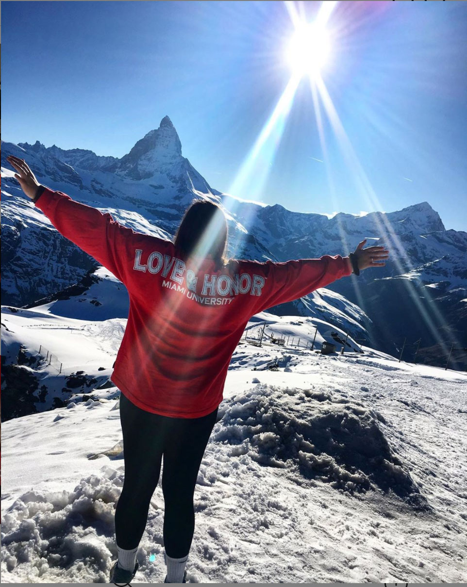 student wearing love and honor shirt faces away from camera and stretches arms toward distant mountains