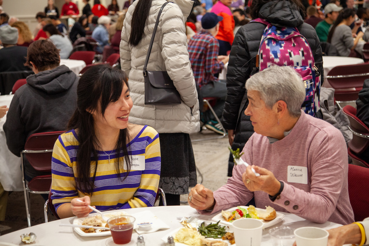 A student and community member chat at the 2019 thanksgiving dinner