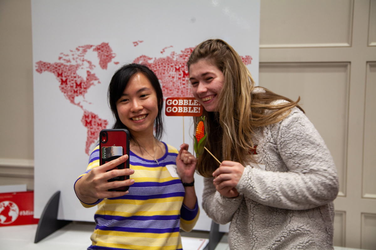 Two students take a selfie in front of an international backdrop