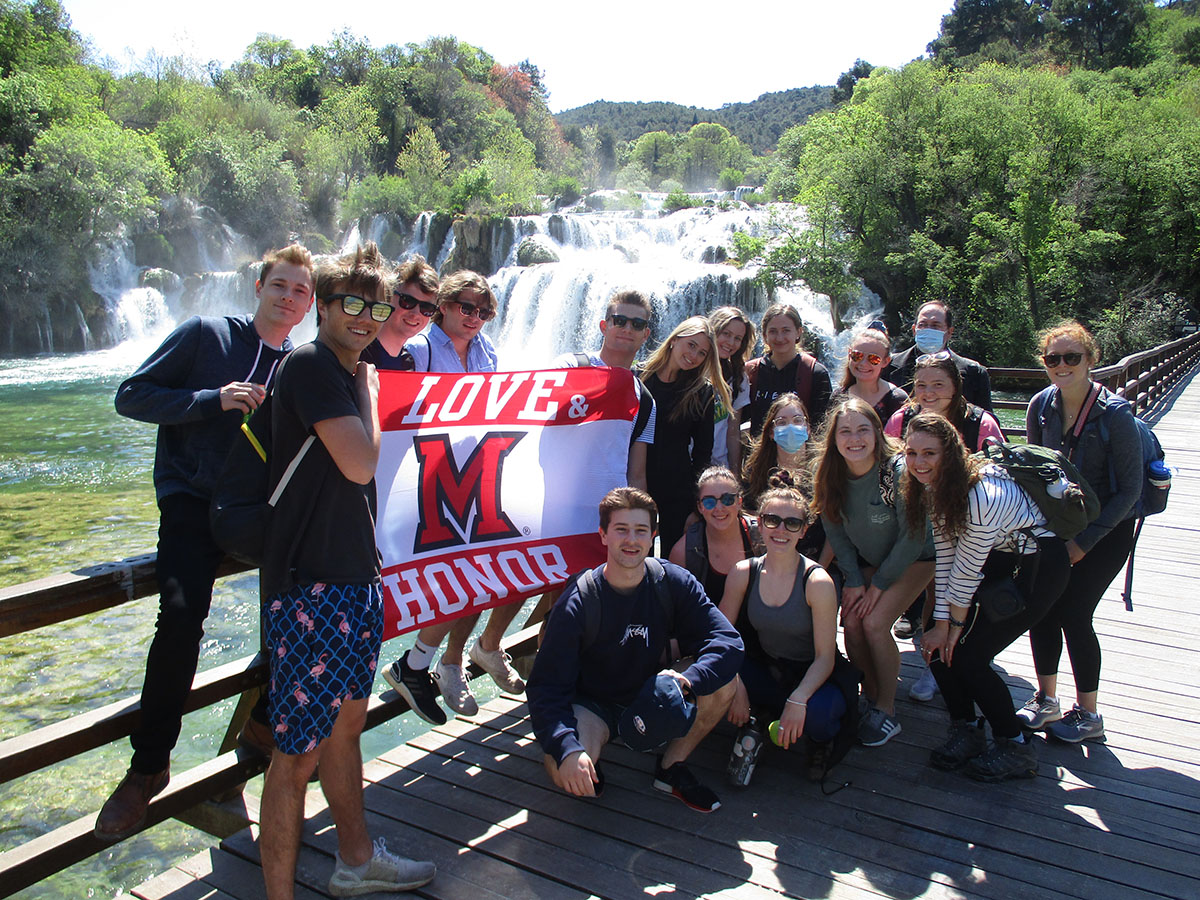 Students studying at MUDEC hold a Miami flag near a waterfall during a study tour in Croatia