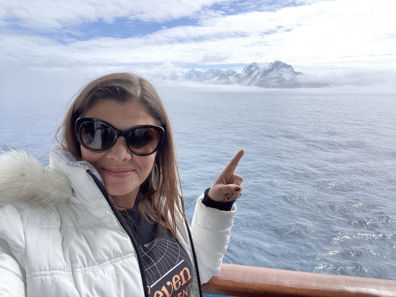 Kimberly Miller, wearing dark goggles and winter apparel, points to the shore of Antarctica