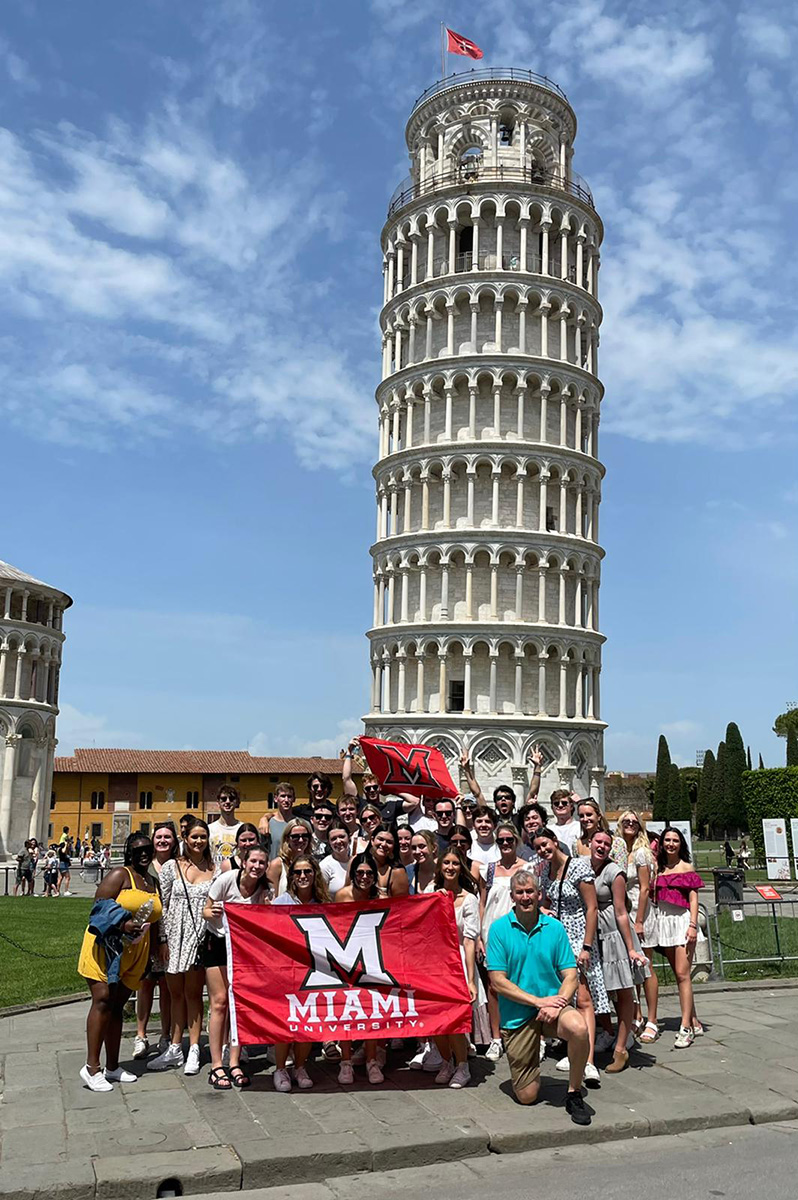 Students pose with an M flag in front of the Tower of Pisa