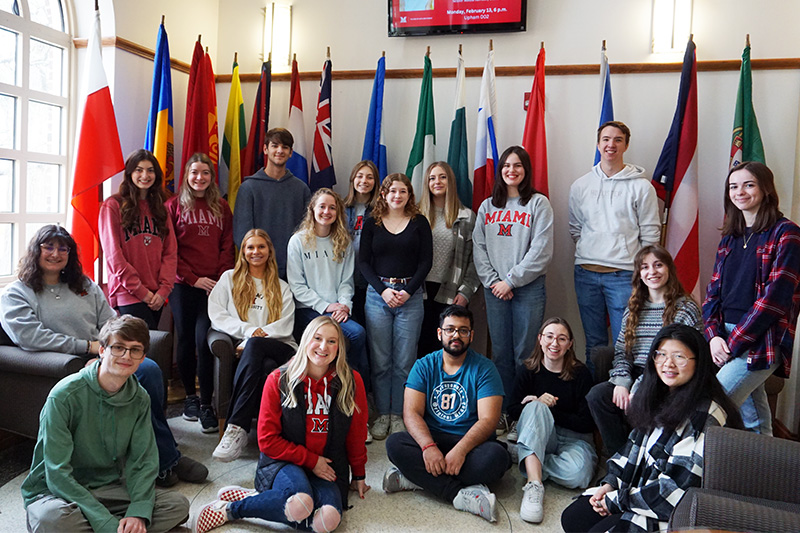 With international flags in the background, CCA cohort poses for a group picture in the lobby of MacMillan Hall