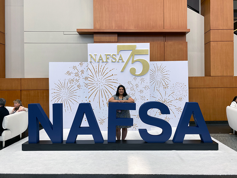 Alicia Castillo Shrestha poses in front of the NAFSA sign