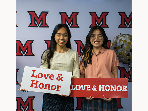 Angel Luo celebrates graduation with roommate Kim Ha. Both students hold signs reading 'love and honor'