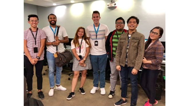 Alexander Wright and six young adults standing and smiling in a brightly lit office, wearing ID badges.