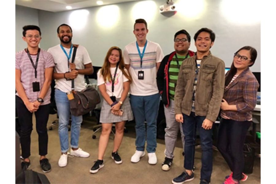 Alexander Wright and six young adults standing and smiling in a brightly lit office, wearing ID badges.