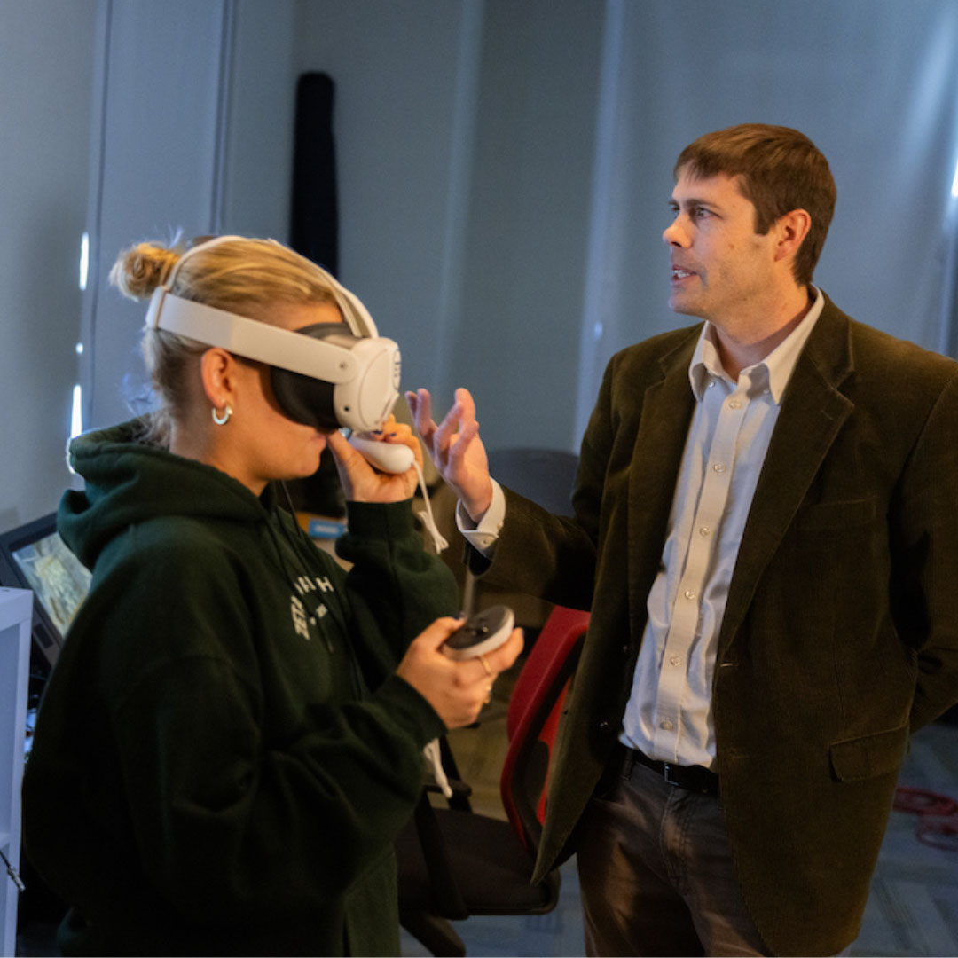 Miami professor Eric Hodgson training student to use virtual reality equipment