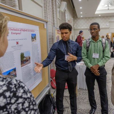 Miami undergraduate students presents their research poster to a visitor at the annual Undergraduate Research Forum