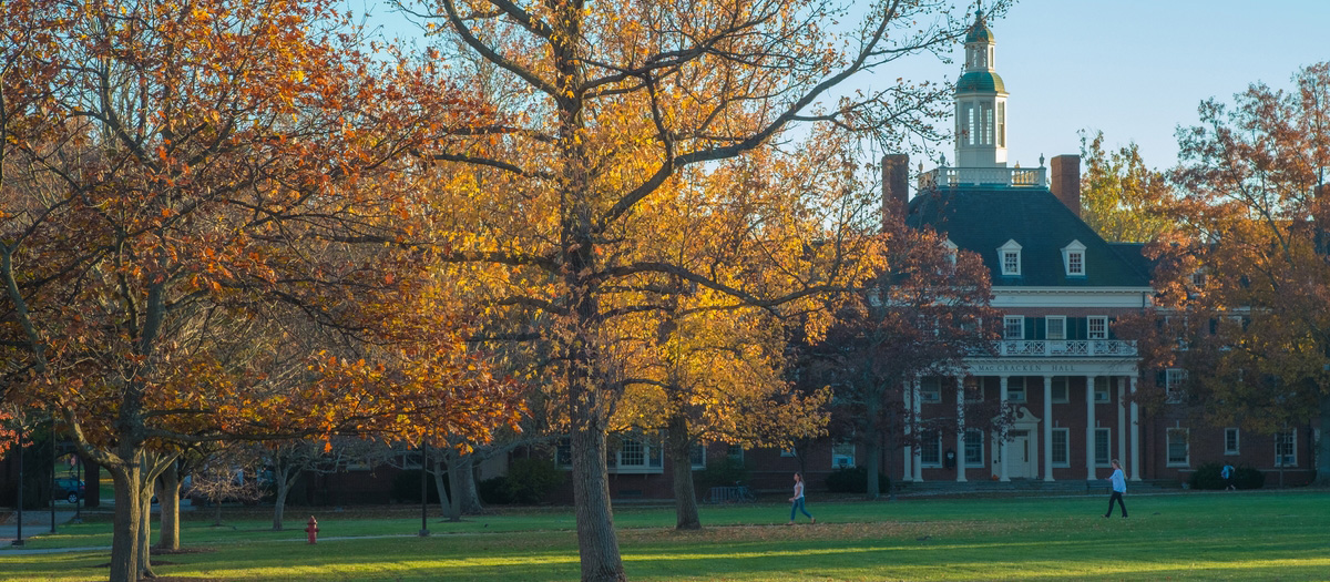 Wide shot of MacCraken Hall in the fall with students walking in past. 