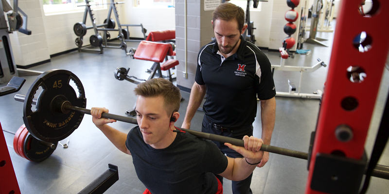 Student lifts weights with the help of a trainer in Martin Fitness Center.
