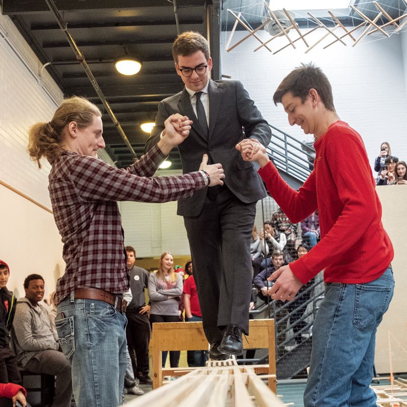 A team of architecture students help their classmate to walk across a makeshift bridge in their classroom