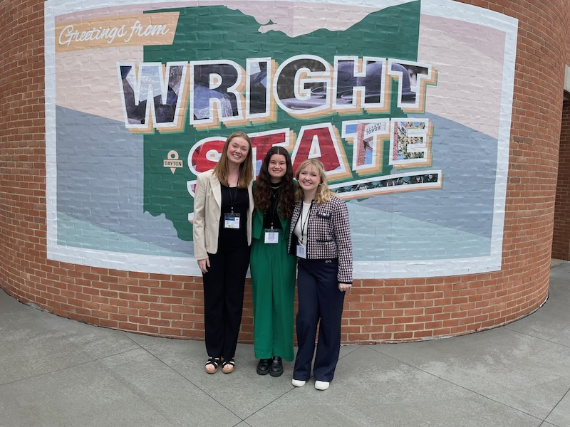 Three consultants standing in front of a Wright State mural outside a building
