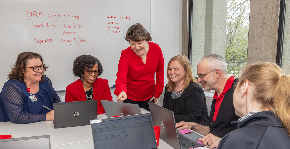 Some members of the Human Resources team working in a conference room with laptops and a whiteboard