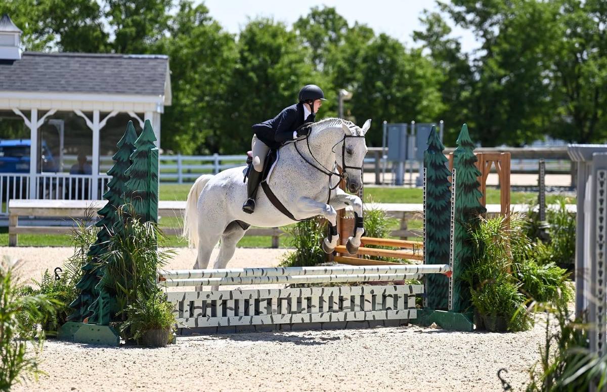 A member of the Miami Equestrian team jumps her horse over a barrier during a competition