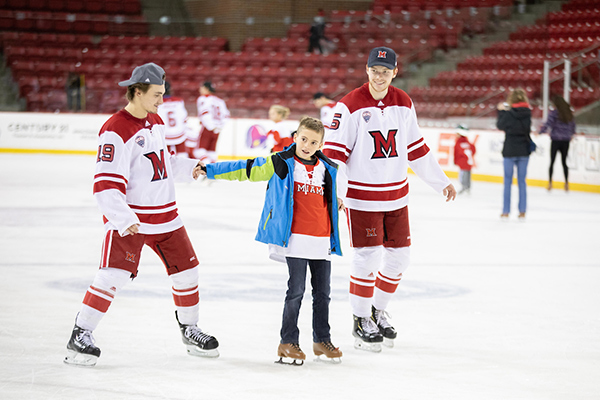 Two Miami University hockey players skating with a young boy.