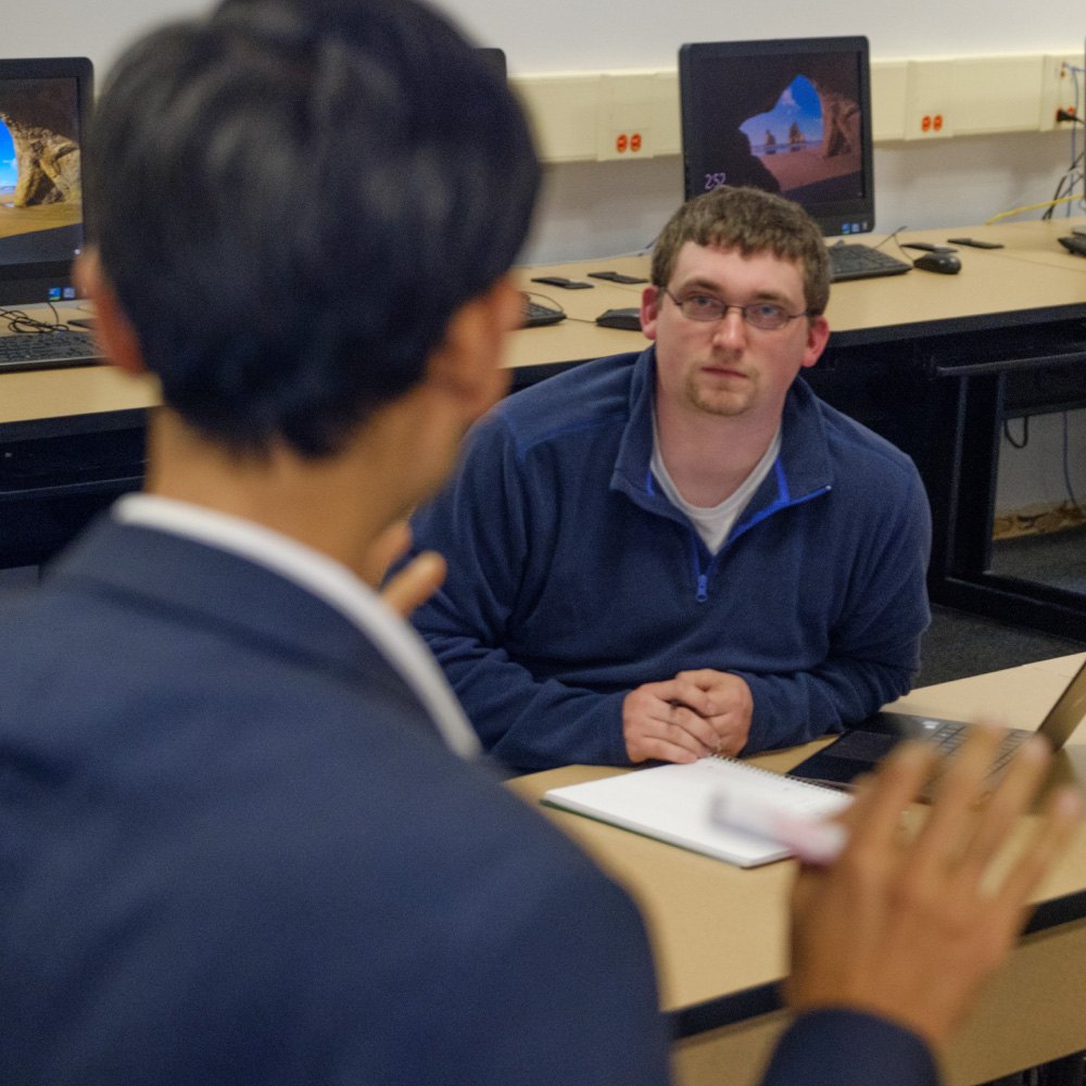 A male student sitting in class listening to his professor. 