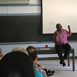 Ron Scott facilitating discussion while sitting on a table in front of a classroom