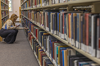 A female-presenting person crouches in front of a wall of books at a library