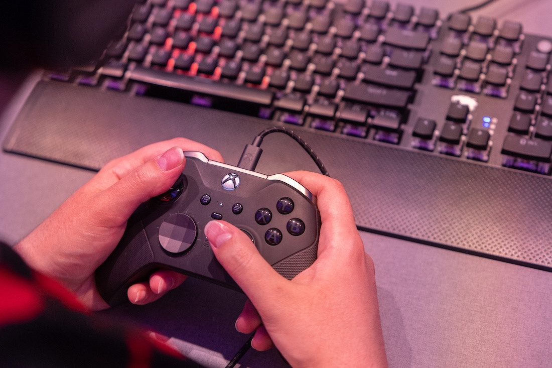Close up of two hands using a video game controller with a computer keyboard in the background