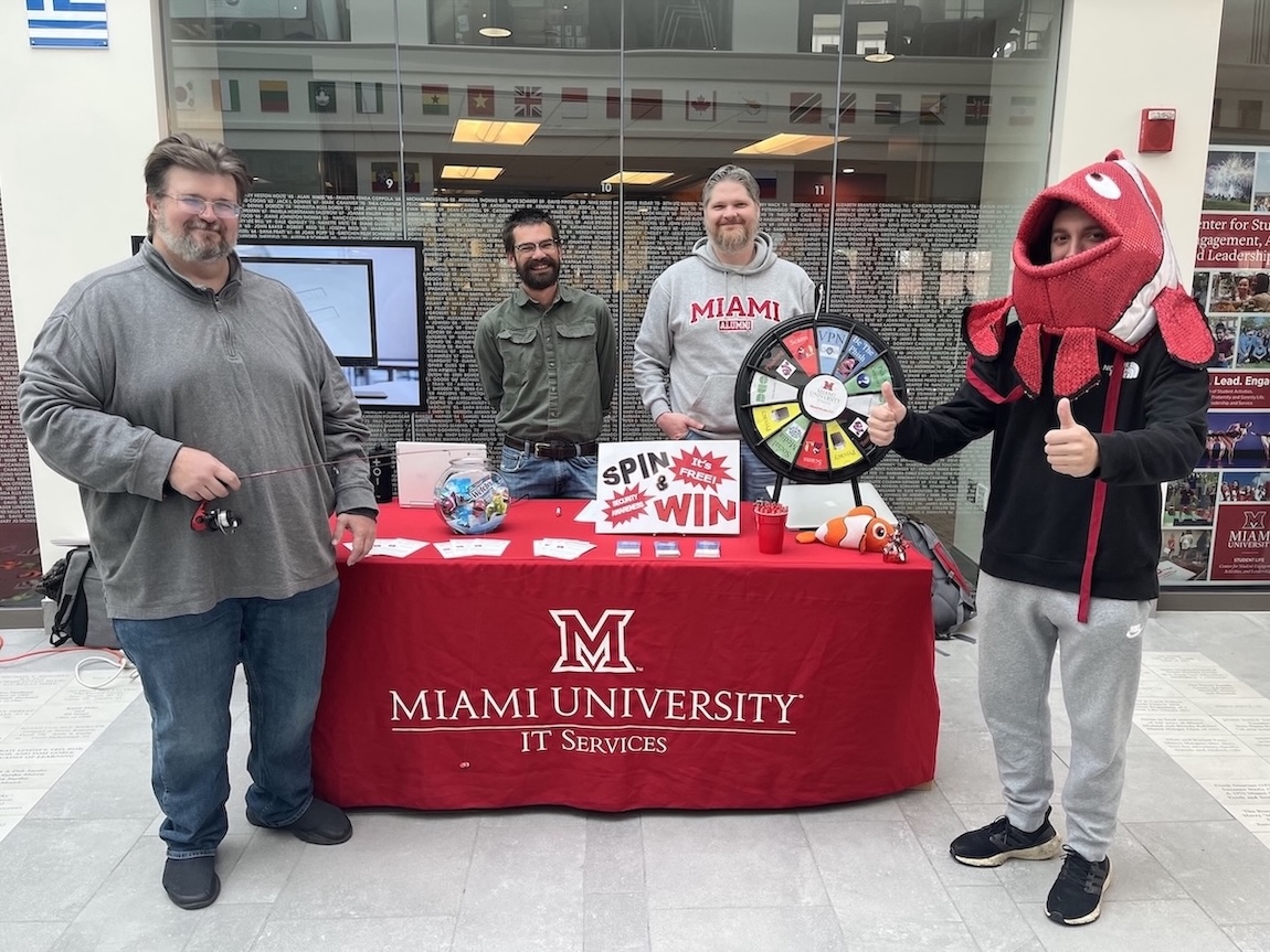Members of the Miami University Information Security team stand next to their information table about cybersecurity awareness in the Armstrong Student Center