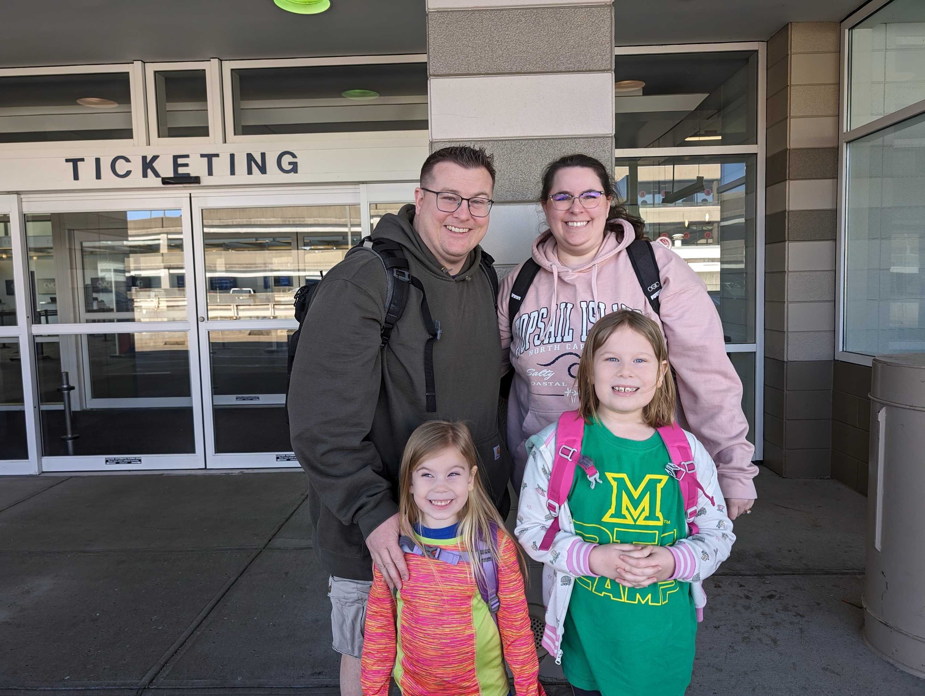 Erin and Joe Mills with their daughters outside a ticketing office for an airport or train station