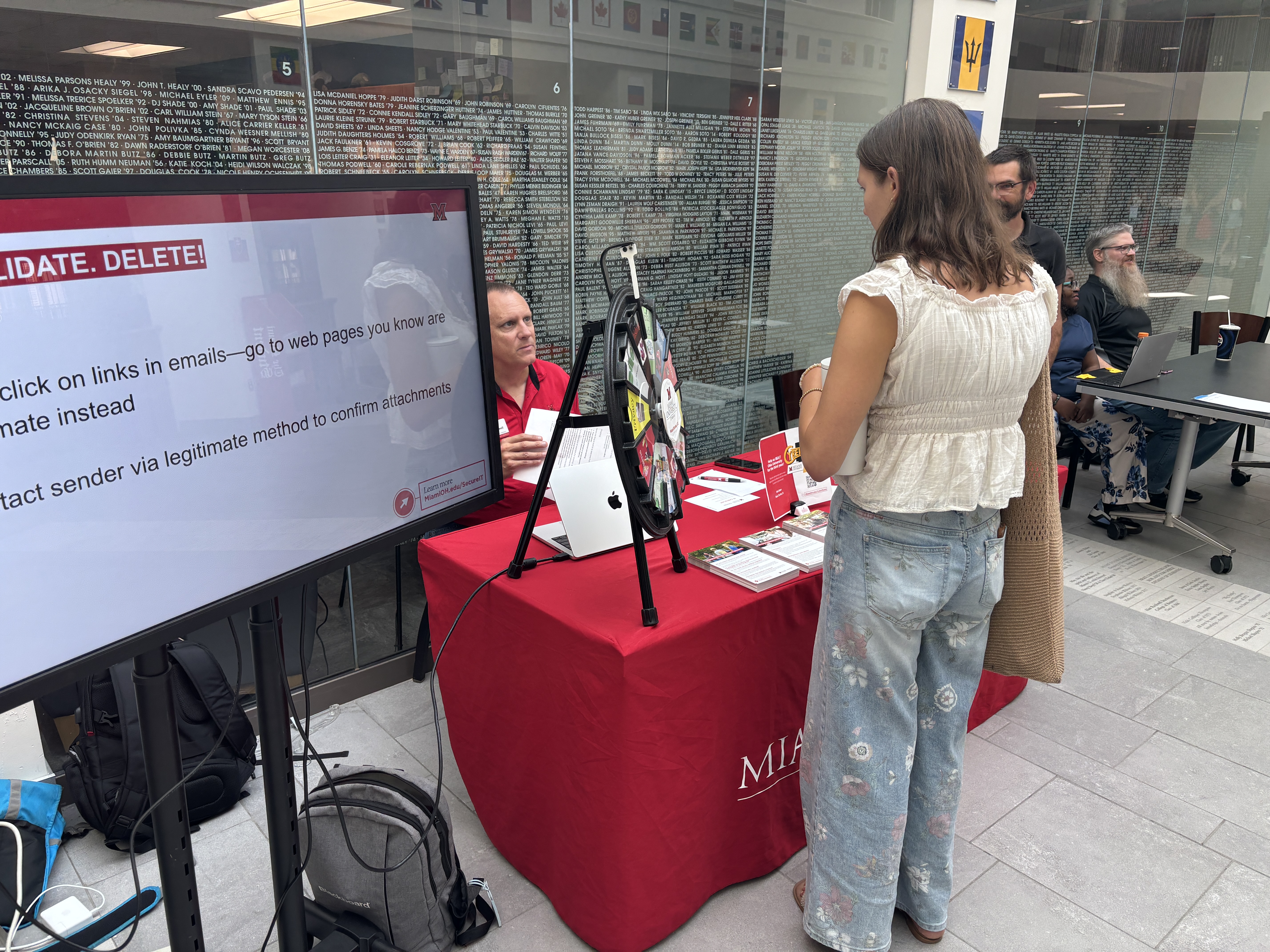 A young person standing in front of the information security awareness table, next to a screen that says 'stop validate delete'