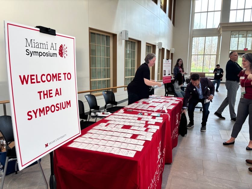 A poster declaring 'Welcome to the Miami AI Symposium' next to the check-in table where attendees grabbed their pre printed name badges.