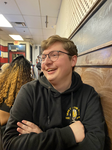 Cameron Paul in a blue hooded sweatshirt leaning against a wall smiling