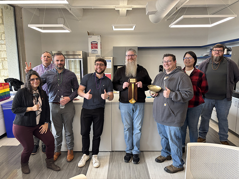 The winners, judges, and emcee for the IT Services chili competition pose for a photo after the event.