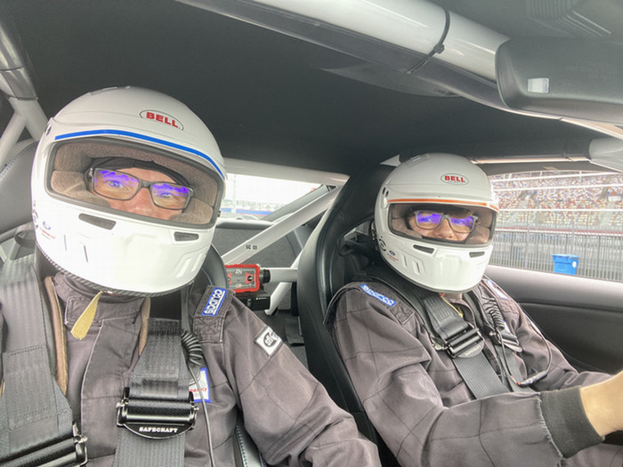 Craig Martin and his son Andrew at the racetrack wearing full face racing helmets. They are sitting in a racecar.