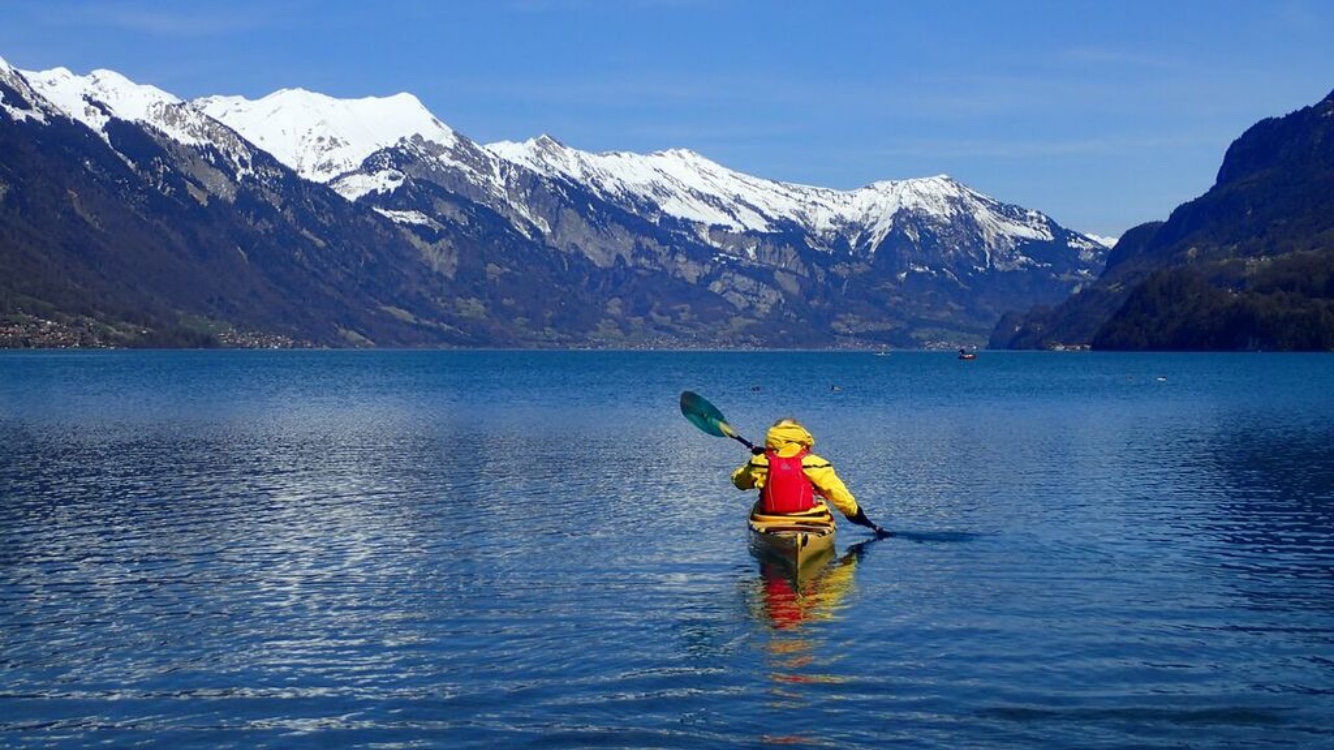 A lone kayaker in a calm lake overlooked by snow capped mountains