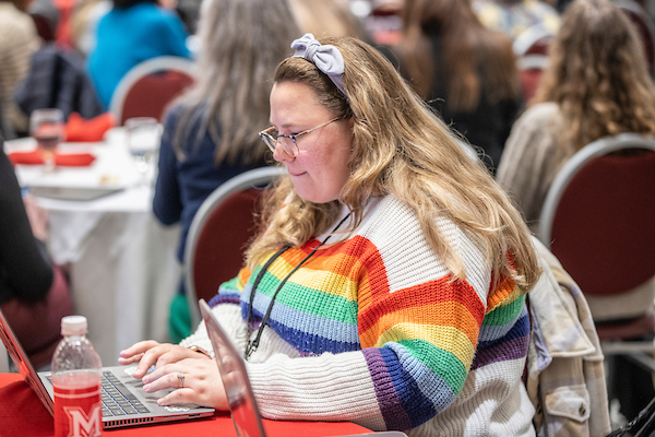 A person on a computer wearing a rainbow sweater