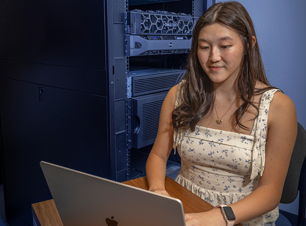 A student employee on a computer. In the background is a server