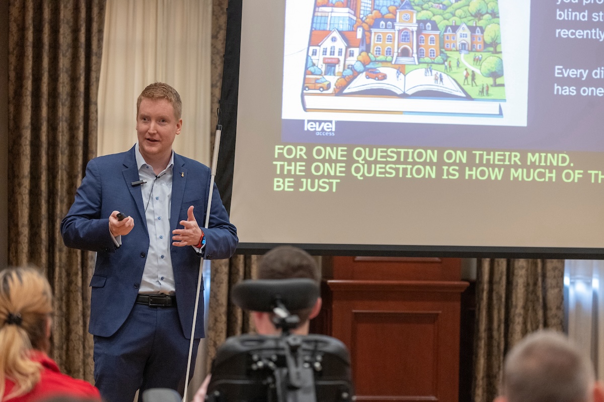 Corbb is speaking adjacent to the screen which displays partial view of captions "For one question on their mind. The one question is how much of"