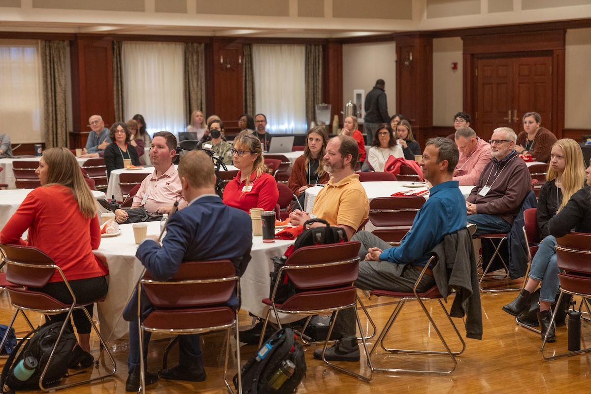 Attendees sit at round tables in the Heritage Room and listen to a presenter