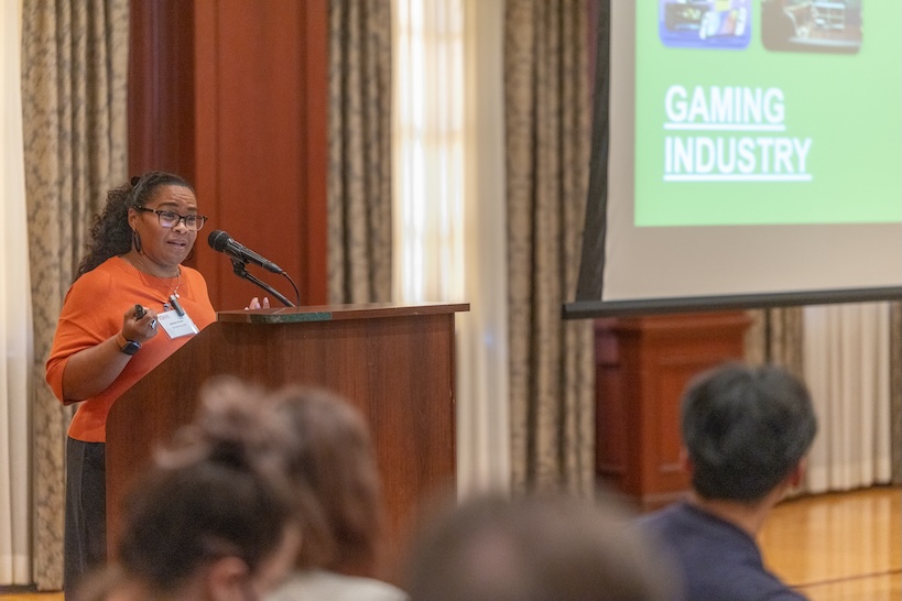 Belinda Worley stands at the podium next to the screen which displays gaming industry slide