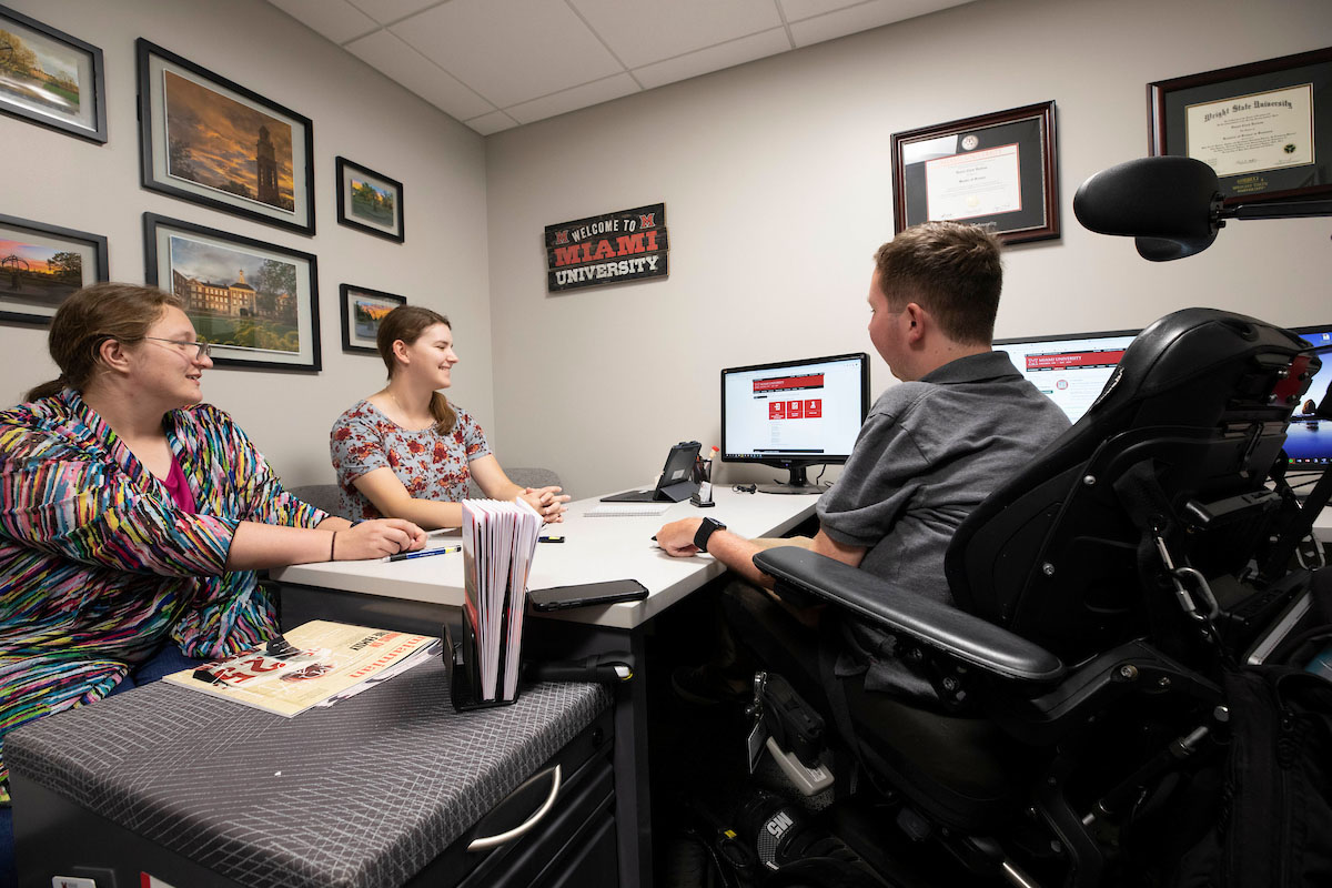 A student in a wheelchair sitting at a desk with Miami staff members
