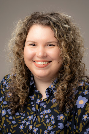 Professional photo of person with long brown hair in a flower shirt and a tan background.