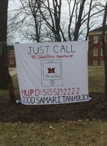 Banner sheet sign hanging between two trees on academic quad. Banner Reads Just Call. 911 Oxford Police Department. MUPD 513-529-2222. Good Samaritan Policy.