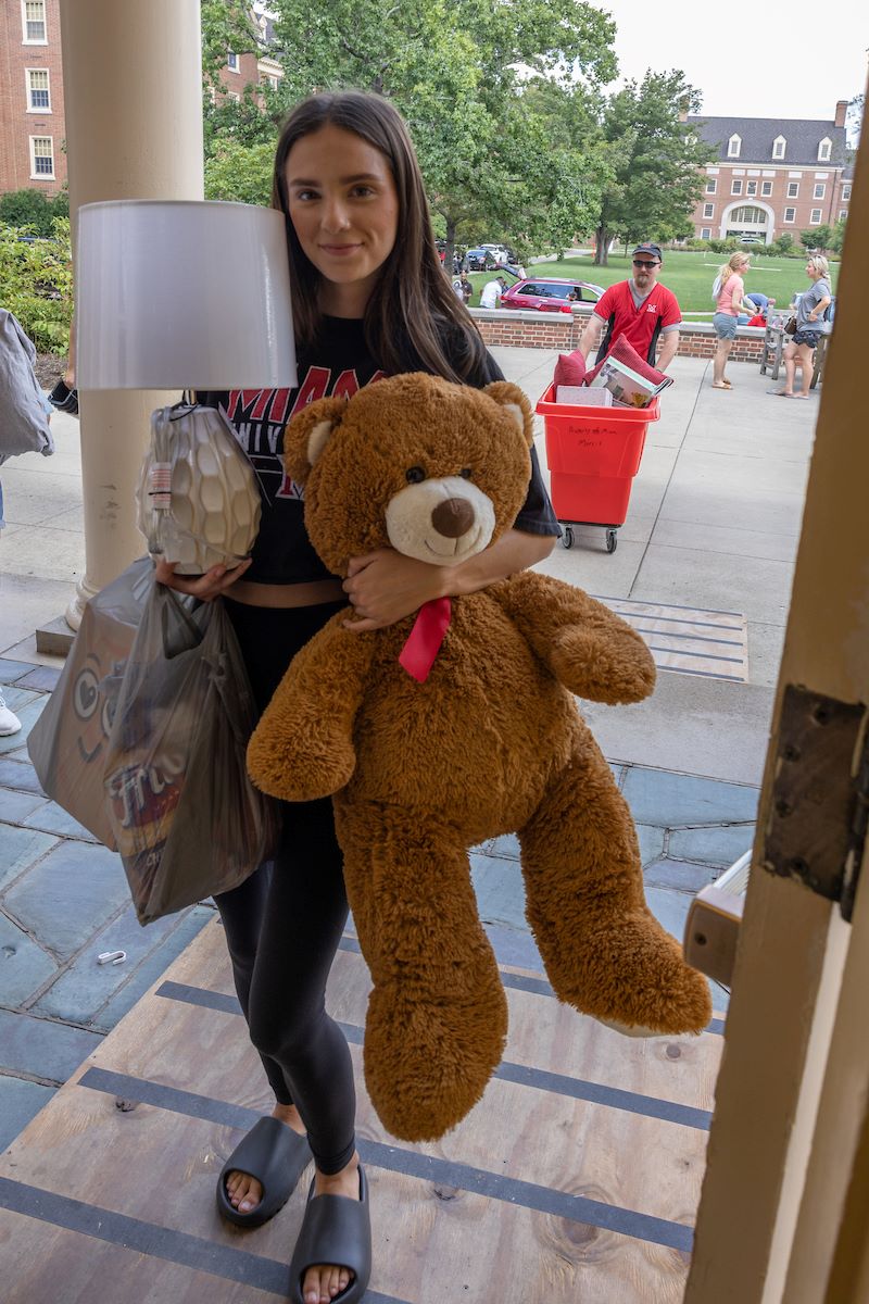 Female student moving into a dorm carrying a large stuffed teddy bear