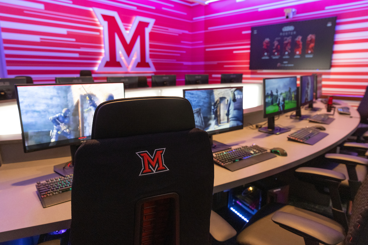 room with comfortable chairs and laptops in a row -the esports room at Miami.