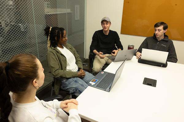 Four students sitting around a table in an Armstrong study room, laptops in front of them. 